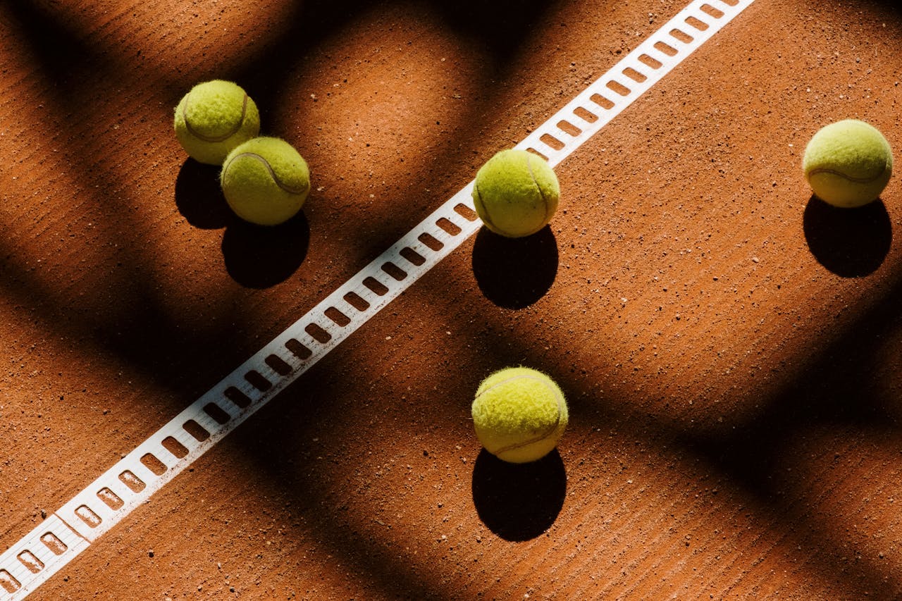 Tennis balls cast shadows on a clay court, showcasing light play and sports ambiance.